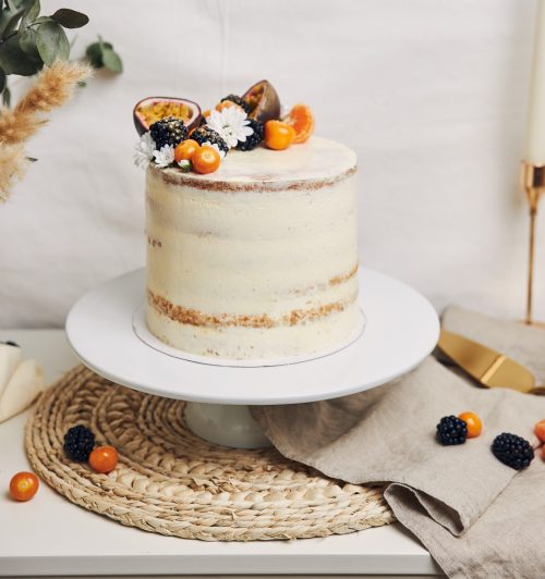 A cake with berries and passionfruits next to a plant behind a white background