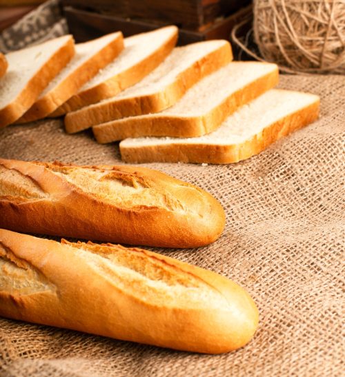 French baguette with slices of bread on tablecloth